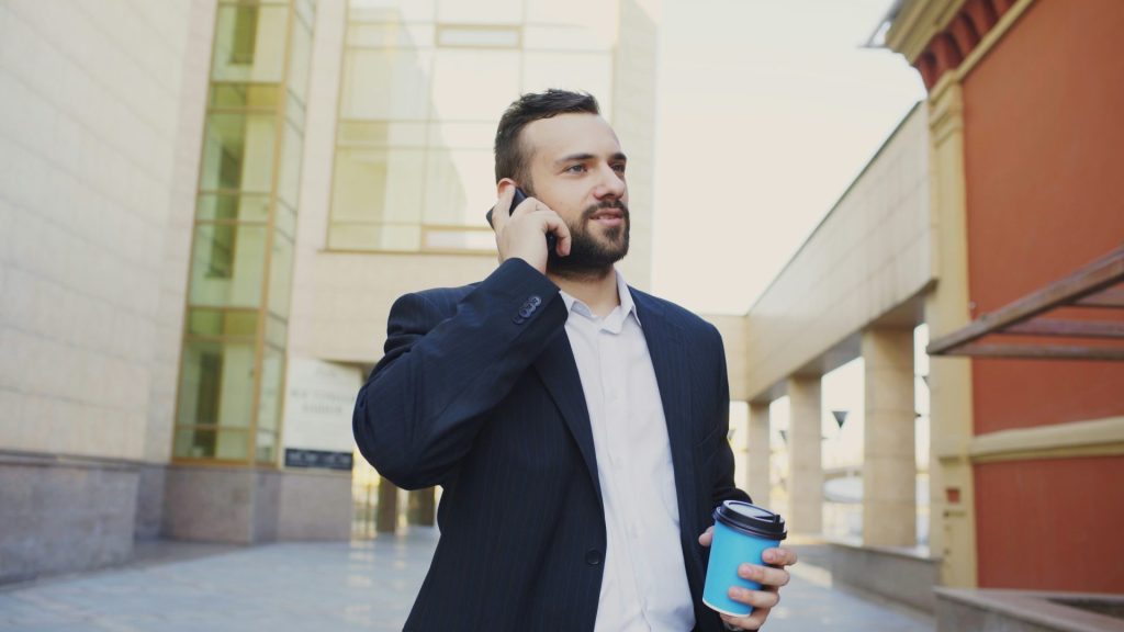 Man in suit talking on phone with coffee cup.